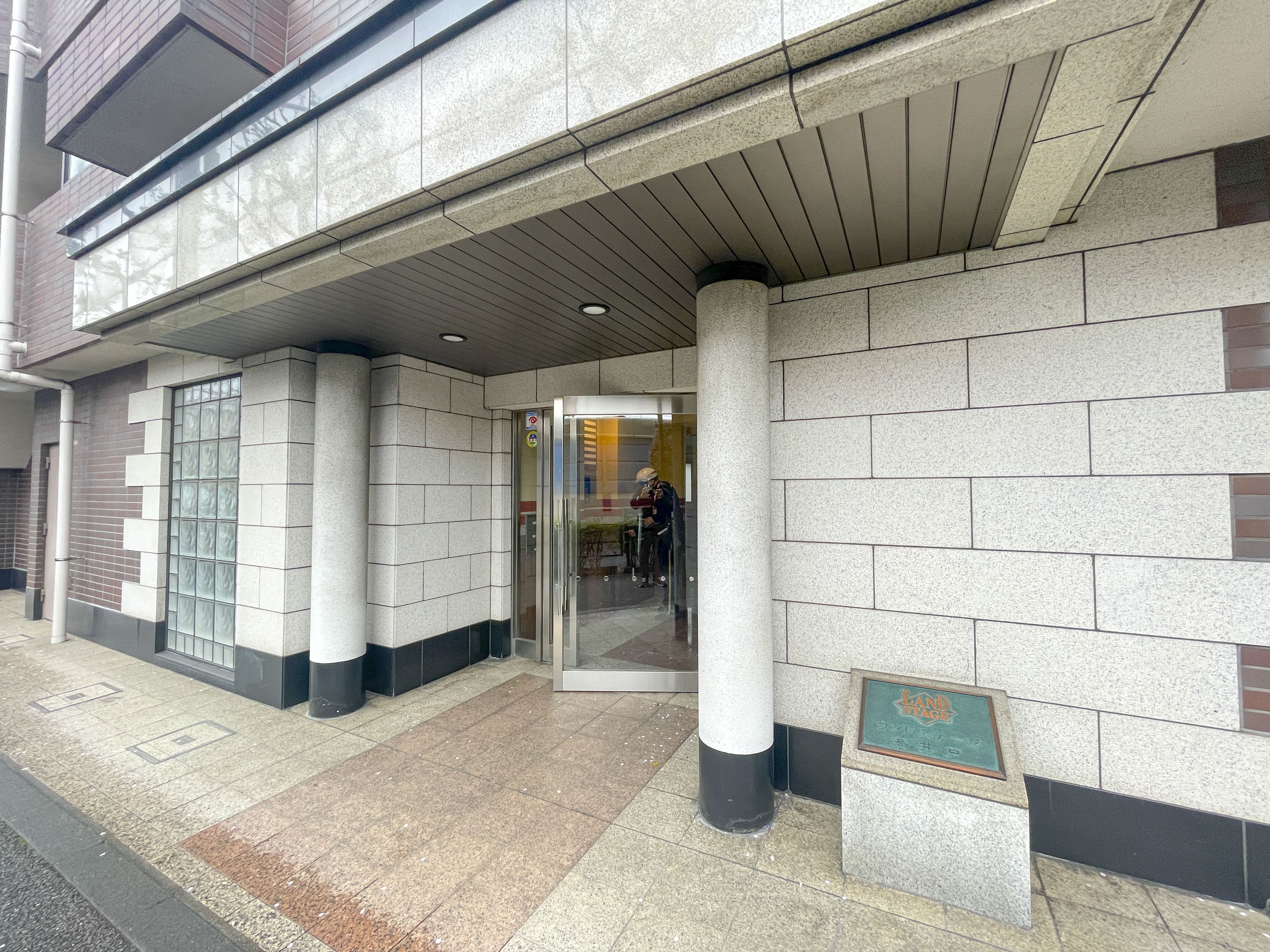 建物の入り口部分、ガラス扉や柱、歩道が主な構成要素の画像