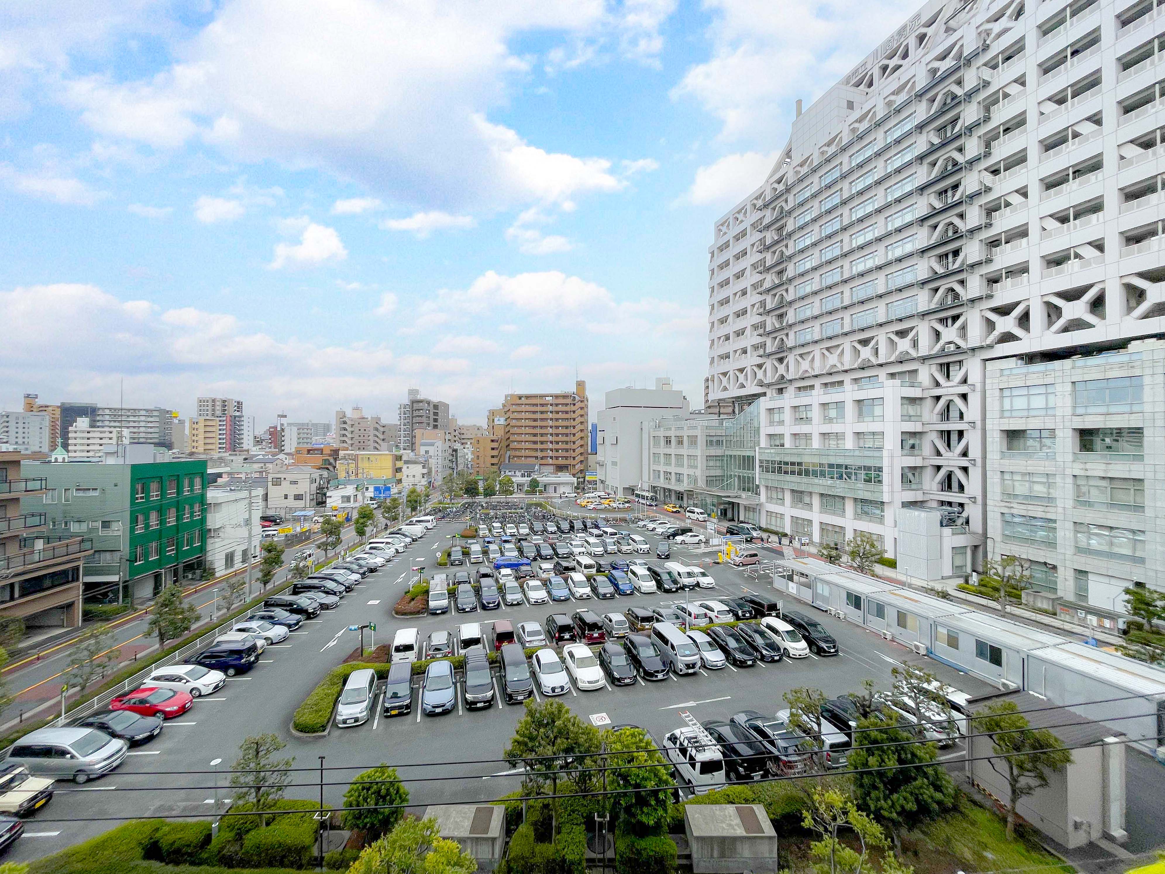 駐車場が中心に写り、多数の車両と周辺の建物を含む画像