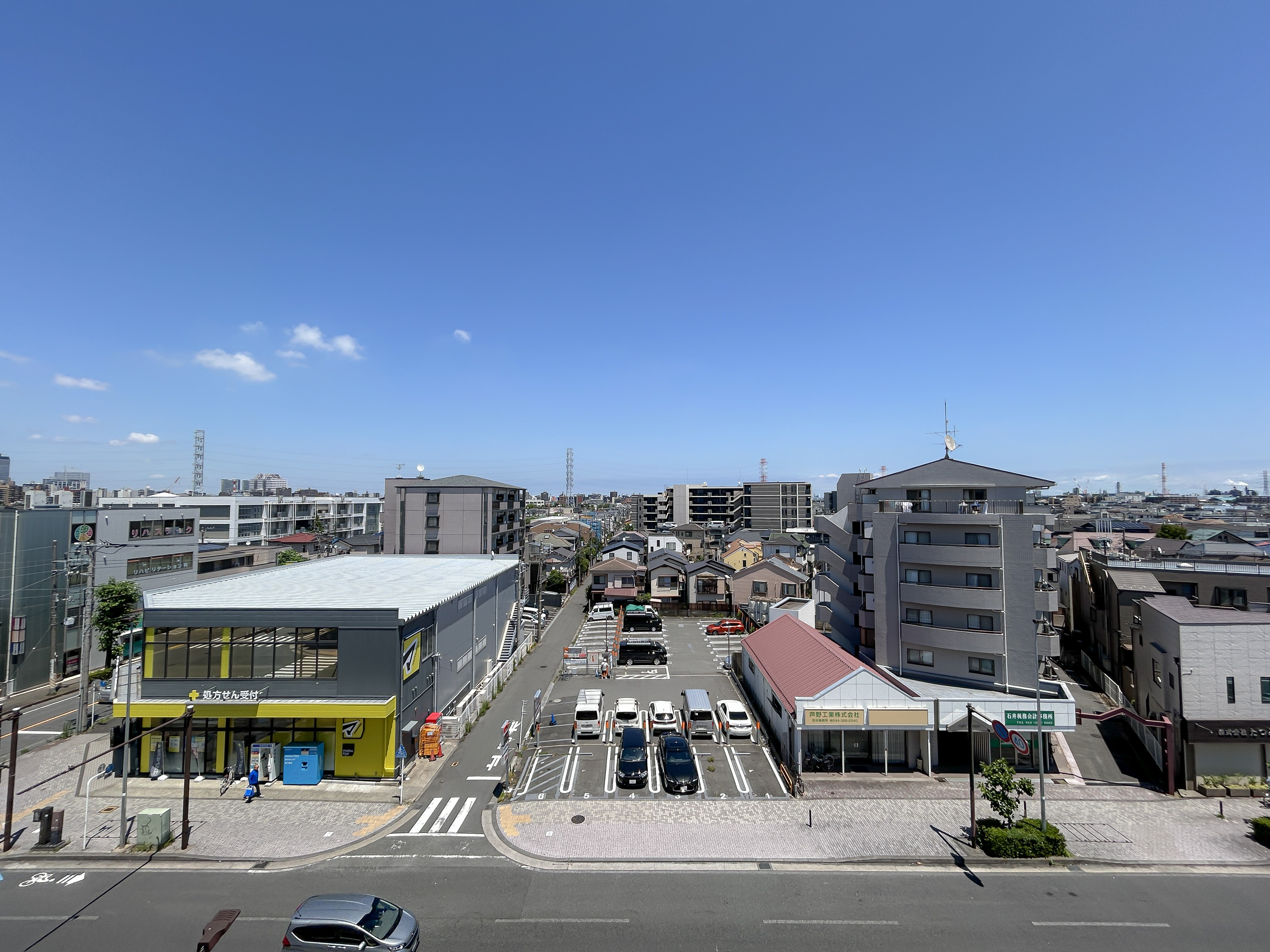 道路、駐車場、周辺建物を含む広範な街並みを捉えた画像